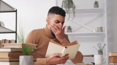 Sıkı eğitim. Erkek öğrenci. Yorgun çalışma. Masada oturup kitap okuyan yorgun bir adam. İç mekânda esniyor..