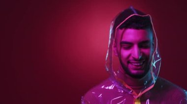 Yağmur koruması. Mutlu adam. Neon ışıklı portre. Yağmurluklu, siber punk tarzı, kırmızı mor arka planlı pozitif hipster..