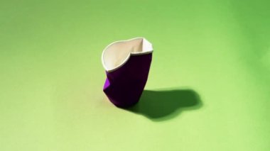 Atık kirliliği. Ekoloji problemi. Çevresel koruma. Yeşil boş alan arka planında kullanılan mor, biyolojik olarak bozunabilir karton bardağın hareketini durdur.