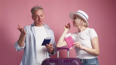 Tatil heyecanı. Mutlu bir çift. Trip belgesi. Pasaportları pembe arka planda olan, bavullu, orta yaşlı kadın ve erkek..