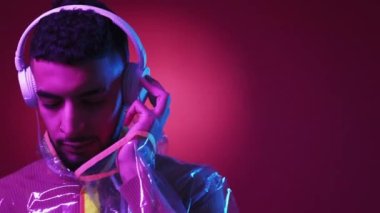 Müzik ilhamı. Siberpunk adam. Neon ışıklı portre. Pozitif hipster adam gözlerini kapattı kulaklıkla şarkı dinliyor kırmızı mor arka plan.