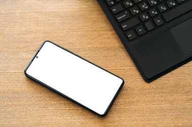 Mobil model. Ofis işleri. Dijital teknoloji. Ahşap masadaki boş ekranlı akıllı telefon dizüstü bilgisayarı düzleştirdi.