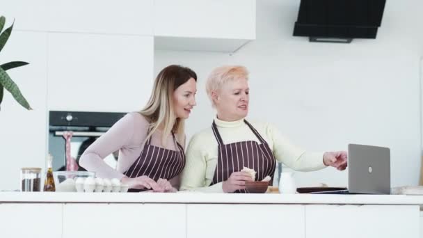 パン屋のブログ 料理をする女性 家族のレジャー 幸せな母親と娘見ますビデオ上のラップトップと作業上のペストリーライトキッチンルームインテリア — ストック動画