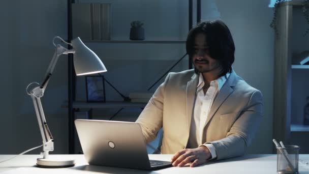 在线会议 笑的人 迟到了英俊而优雅的男人 坐在笔记本电脑桌前 低着头 坐在黑暗的灯光下 — 图库视频影像