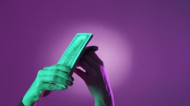 Profesyonel muhasebeci. Zengin biri. Paranın tadını çıkarıyorum. Kadın eli, neon ışıklı mor arka planda yığınla para sayıyor..