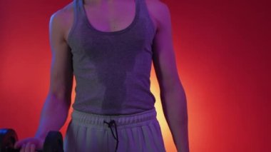 Güç kaldırma sporu. Neon ışıklı adam. Sıkı antrenman. Tanımlanamayan, ıslak yelekli terli adam sarı arka planda dambıllarla egzersiz yapıyor..