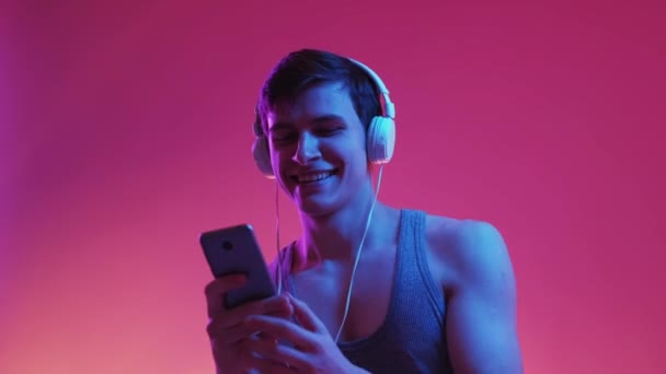 ダンスマン ネオンの肖像画 モバイル音楽 幸せな面白いです男でヘッドフォン移動でリズムホールディングスマートフォン上の青紫色の背景 — ストック動画