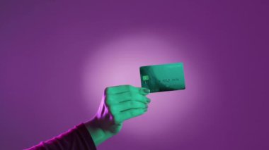 Banka ödemesi. Para müsrif. Sınırsız finans. Neon açık mor arka planda kredi kartı gösteren bir kadın el..