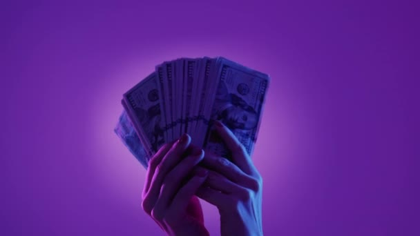 大きな利益だ 金持ちだ お金を数える ネオンライトパープルブルーの背景にドルの現金の山を示す女性の手 — ストック動画