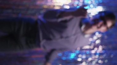 Dikey video. Neon ışıklı parti. Odaklanamayan mutlu adam. Şenlikli gümüş şelale dekorasyonu bulanıklığında dans eden eğlenceli, heyecanlı adam..