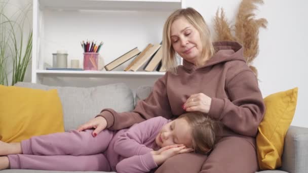 家庭护理 睡梦中的女孩回家休息 笑容满面的慈祥老奶奶哄着小孩坐在沙发上轻柔的房间里抚摩着头发 — 图库视频影像