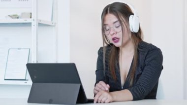 Çevrimiçi görüşme. Sanal toplantı. Mesafe iletişimi. Kendine güvenen kulaklıklı bir iş kadını modern dijital ofiste boş yeri olan tablet kullanıyor. Uzun video çekimi.