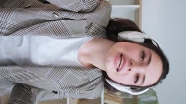 Dikey video. Uzaktan antrenörlük. Sanal görüşme. Mesafe eğitimi. Kulaklıklı, kendine güvenen, selamlayan, selamlayan ve internette konuşan bir kadın..