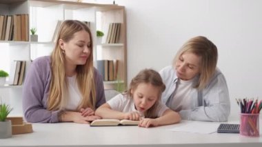 Okuma ödevi. Meraklı kız. Destekleyici aile. Anne ve büyükanne, sevimli çocuğun yeni kitap çalışmasına yardım ediyor..