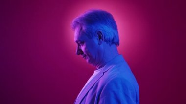 Neon ışıklı yaşlı adam. Profil portresi. Şık bir görünüş. Gülümseyen yaşlı bir erkek, mavi arka plan halesi üzerinde poz veriyor..