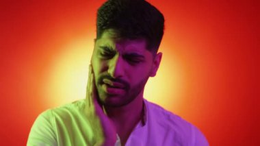 Diş ağrısı çekiyor. Endişeli adam. Neon ışıklı portre. Mor turuncu arka planda acı hisseden gergin hasta bir adam..