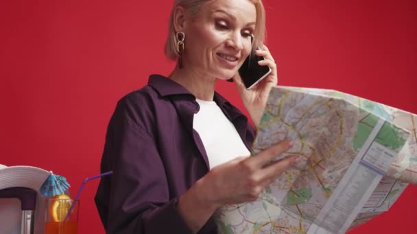 选择目的地 快乐的女人移动信息 笑容可亲的女士在讲智能手机 讨论在地图上展示红色背景的旅行方向 — 图库视频影像