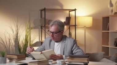 Araştırma bilgileri. Erkek öğretmen. Ders hazırlığı. Meraklı, zeki, yaşlı bir adam kitap okuyor aydınlık karanlık odada masa başında oturuyor..