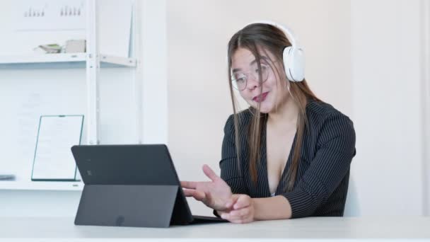 オンライン通話 インターネット会議 遠隔通信だ ヘッドフォンの陽気なビジネス女性は 仮想オフィスでタブレットを使用して仕事を議論します 長いビデオショット — ストック動画