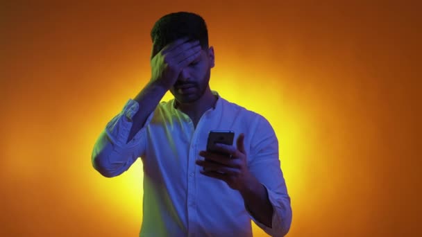 手机游戏 绝望的男人 霓虹灯肖像 可悲的家伙看着智能手机 后悔摆出紫色橙色的背景 — 图库视频影像