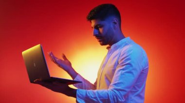 Bilgisayar sorunu. Kızgın adam. Neon ışıklı portre. Mor turuncu arka plan pozu veren memnun olmayan adam laptopta giriş yaparken başarısız oluyor..