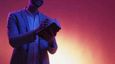 İlginç bir bilgi. Meraklı adam. Neon ışıklı portre. Tanımlanamayan mutlu adam not defterine not alıyor. Mavi sarı arkaplan fotokopi alanı üzerine poz veriyor..