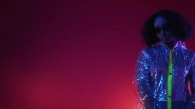 Sıkıcı parti. Üzgün kadın. Neon ışıklı portre. Kırgın bayan güneş gözlüklü şık yağmurluklu kırmızı arka plan fotokopi alanı kalıyor..