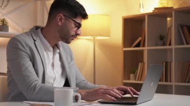 Online iş. Meşgul adam. Dijital teknoloji. Klasik takım elbiseli ciddi bir adam dizüstü bilgisayarını kontrol ediyor masa lambası odasının içindeki belgeleri kontrol ediyor..