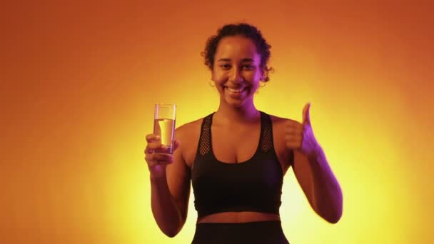 水平衡 霓虹灯的女人 健康的生活方式身穿运动服的快乐女士举着一杯清澈的饮料 摆出一副红黄相间的姿势 — 图库视频影像