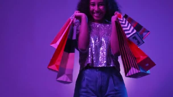 假日购物 兴奋的女人打折销售 快乐漂亮的女士 带着色彩艳丽的纸袋 背景是紫色 霓虹灯 — 图库视频影像