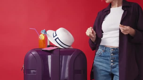 假期快乐 自信的女人夏天的灵感快乐而难以辨认的女士在行李箱边跳着鸡尾酒 戴着红色背景的夏帽 — 图库视频影像