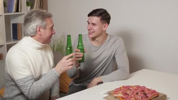 家族関係だ 肯定的な男性 ホームレジャー 幸せな父と息子のビールを飲みながら座っている机とピザで光の部屋のインテリア — ストック動画