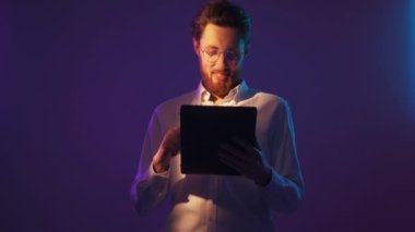 Ağ araştırması. Mutlu adam. Neon ışıklı portre. Gülümseyen zeki adam tablet bilgisayarı kaydırıyor menekşe ışığı aksanı yapıyor..