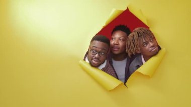 Curious black men. New place. Wow effect. Portrait of shocked male friends looking from yellow disrupted paper on red background copy space.