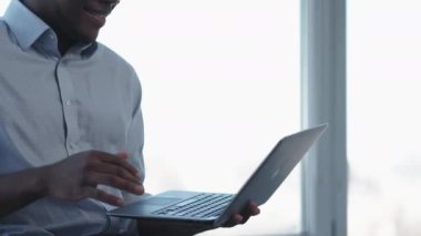 Dijital iş. Çevrimiçi iletişim. Bilgi teknolojisi. Aydınlık ofis penceresinde çalışan ve kopyalama alanı olan dizüstü bilgisayar kullanan tanınamayan bir adam.