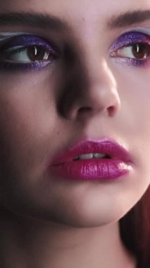 Dikey video. 90 'ların yüzü. Sanatsal makyaj. Eski moda görünüş. Mor renk göz farı olan genç kızın yakın plan portresi. Pembe dudaklar. 2000 'lerin retro güzellik suratı..