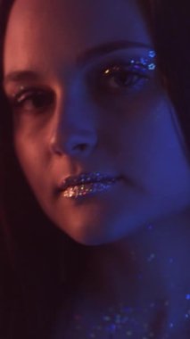 Dikey video. Neon portresi. Parlak makyaj. Gece kulübü güzeli. Pembe mavi renkli, açık renkli, parlak tenli, koyu renk dudaklı kadın yüzü..