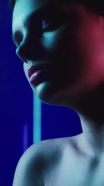 Dikey video. 90 'ların görünüşü. Neon modası. Disko 2000 'in güzelliği. Artistik makyajlı, kapalı gözlü, koyu renk üzerinde kırmızı mor renkte parıldayan rahat genç kız modelinin yakın çekimi..