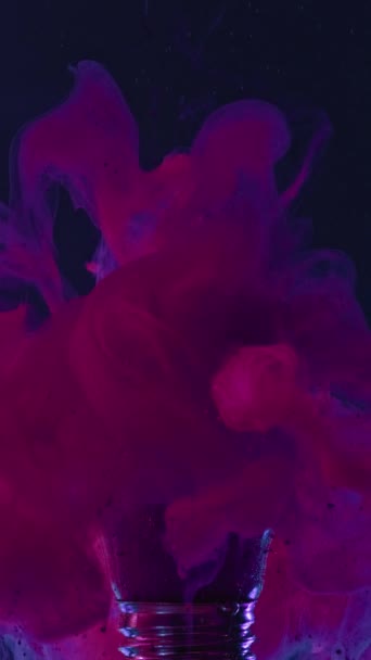 垂直ビデオ 煙が出る インクスプラッシュ 濃い青の抽象的な背景に水の中の壊れた電球からマゼンタピンクの蒸気雲の流れの動き — ストック動画