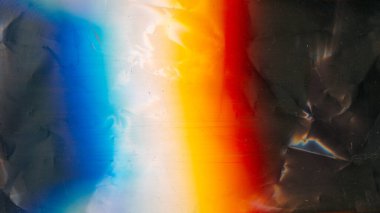 Aged film texture. Dust scratches noise. Weathered foil. Orange blue white rainbow color light flare on dark crushed grunge abstract background.