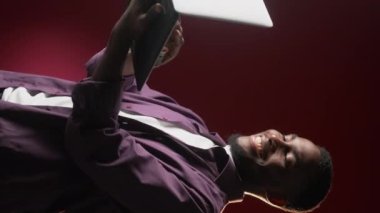 Vertical video. Digital people. Online communication. Information technology. Successful cheerful man using laptop on dark red free space.