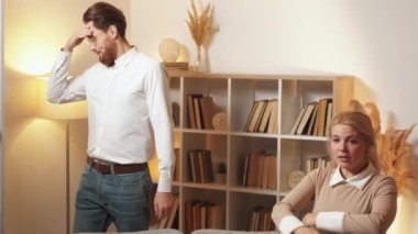 Problem relationship. Couple quarrel. Family misunderstanding. Angry woman rebelling on husband sitting sofa in light shadow room interior.