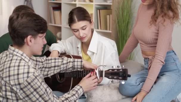 音楽教育 女性の初心者 友達の助けだ 気をつけて男ショー好奇心の女性どのようにギターを演奏ホームパーティーライトルームインテリア — ストック動画