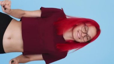 Vertical video. Happy dance. Good mood. Success celebration. Joyful amused smiling girl having fun on blue background seamless loop.