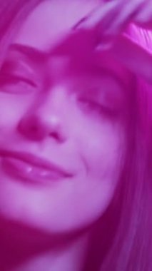 Kadın güzelliği. Neon ışıklı parti. Dansın tadını çıkarıyorum. Pembe bulanık parıltılı, sevimli mutlu kadın ağır çekimde müziğe devam ediyor. Dikey video.