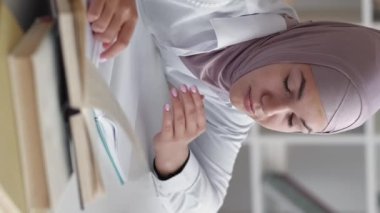 Vertical video. Tired student. Study fatigue. Education insomnia. Exhausted sleepy lazy woman in hijab taking nap waking up at workplace with books.