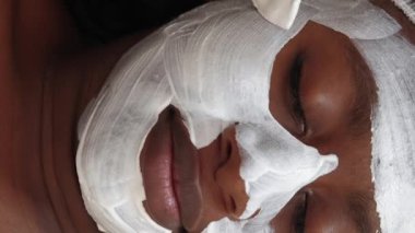 Vertical video. Beauty procedure. Female client. Skincare treatment. Beautician hand applying moisturizing mask on woman face with brush.