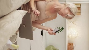 Vertical video. Bank payment. Satisfied woman. Online transfer. Concentrated middle-aged lady typing verification code of credit card in laptop in light room interior.
