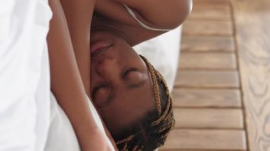 Vertical video. Morning nap. Lazy Sunday. Healthy rest recreation. Relaxed woman with closed eyes sleeping lying in bed in light home bedroom.