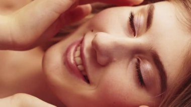 Vertical video. Facial beauty. Pleased woman. Moisturizing nutrition. Smiling pretty lady enjoying tenderly touching face with finger .